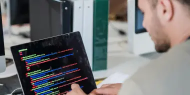 Person working on a tablet displaying colorful programming code in a software development environment.
