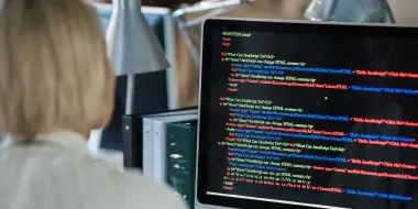 Person viewing a computer screen displaying colorful lines of code in a dimly lit office.