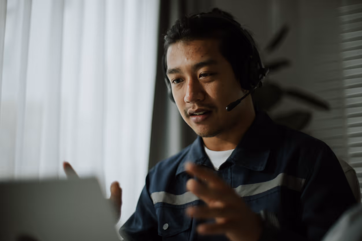 Man wearing headset speaking and gesturing while looking at a laptop in a dimly lit room.