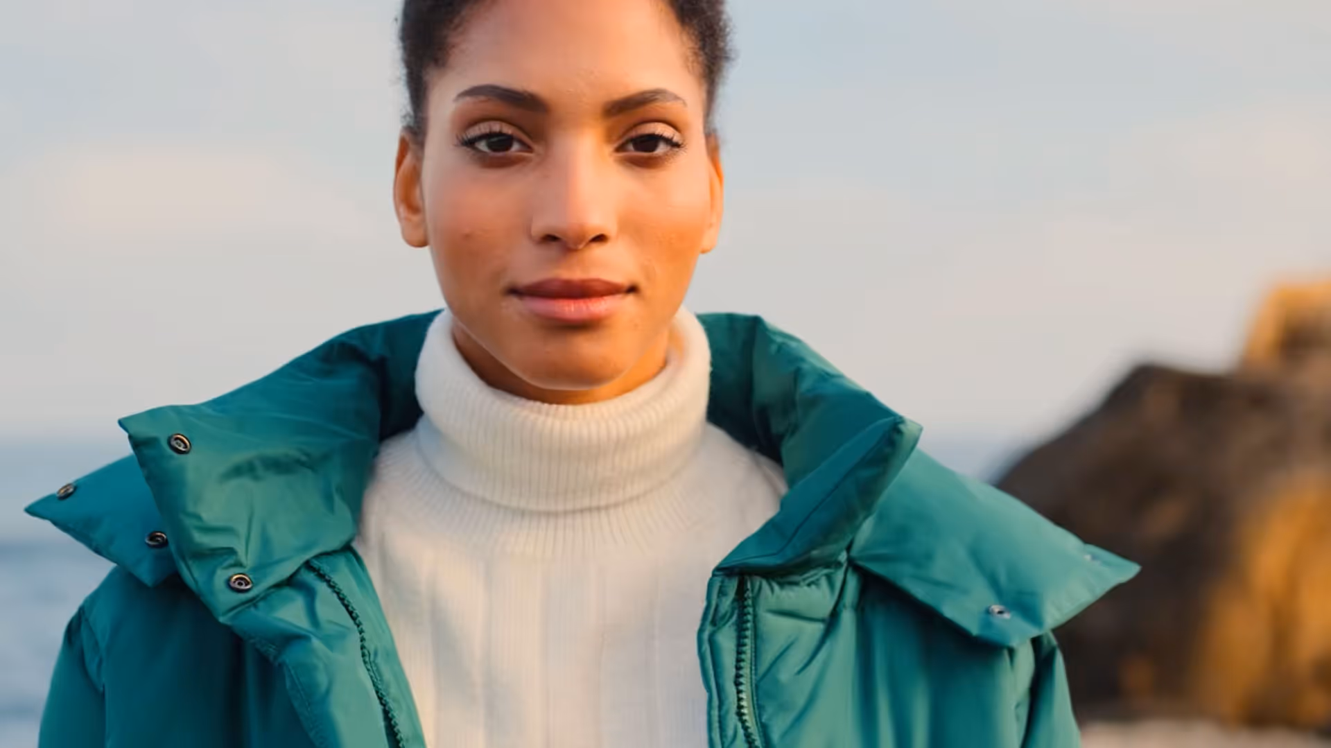 A woman in a green jacket standing by the ocean.