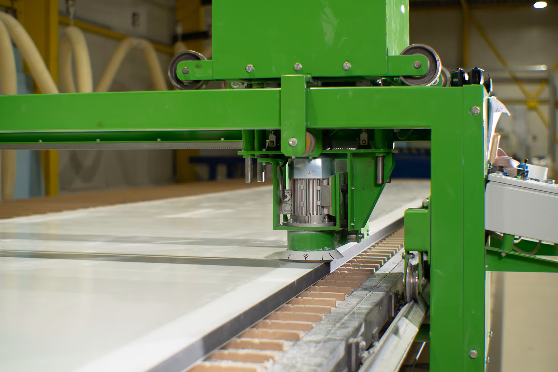 Green industrial machine cutting or processing a large slab of material on a conveyor in a factory.