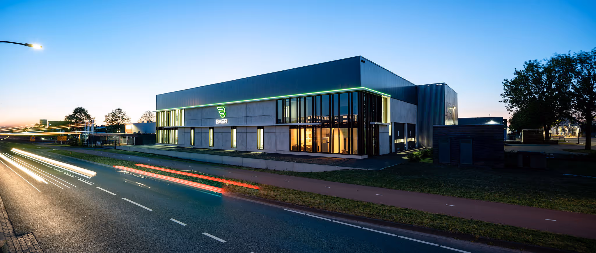 Modern Baer company building at dusk with illuminated logo and light trails from passing cars.