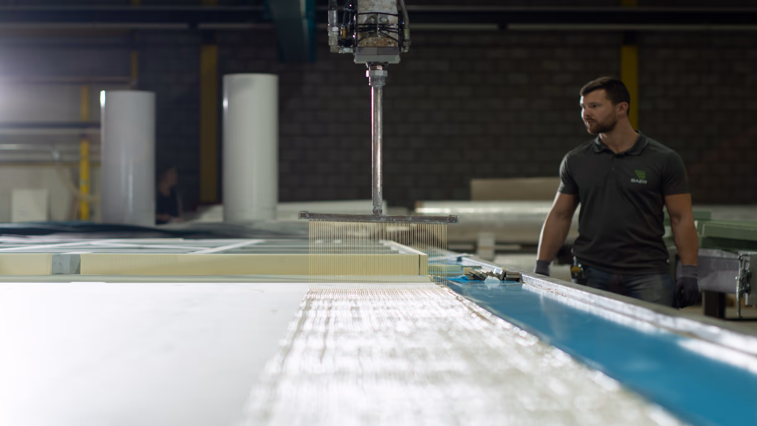 Man in gloves monitoring automated machine applying fine wires or fibers on a production line.