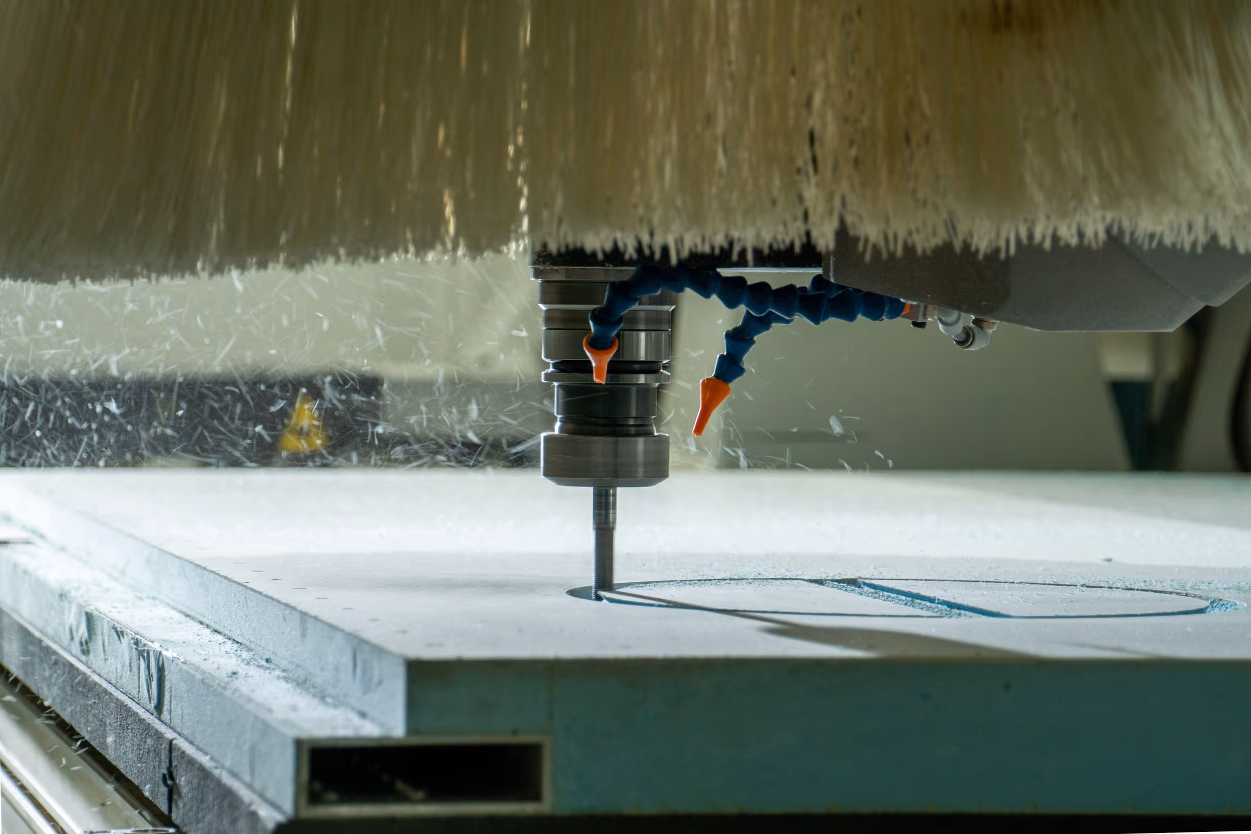 CNC machine cutting a pattern on a flat stone or metal slab with coolant spray.