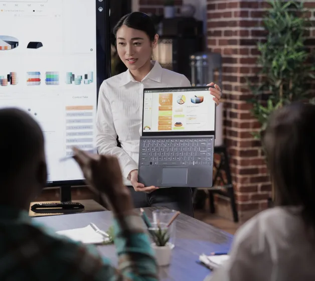 Woman presenting data charts and graphs on a laptop to colleagues in a meeting room.