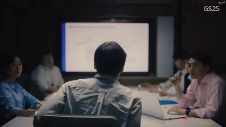 Group of five people in a dark meeting room engaged in a presentation with a screen displaying a map at the front.