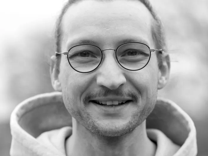 Black and white portrait of Frank Zimmermann, wearing glasses and smiling.