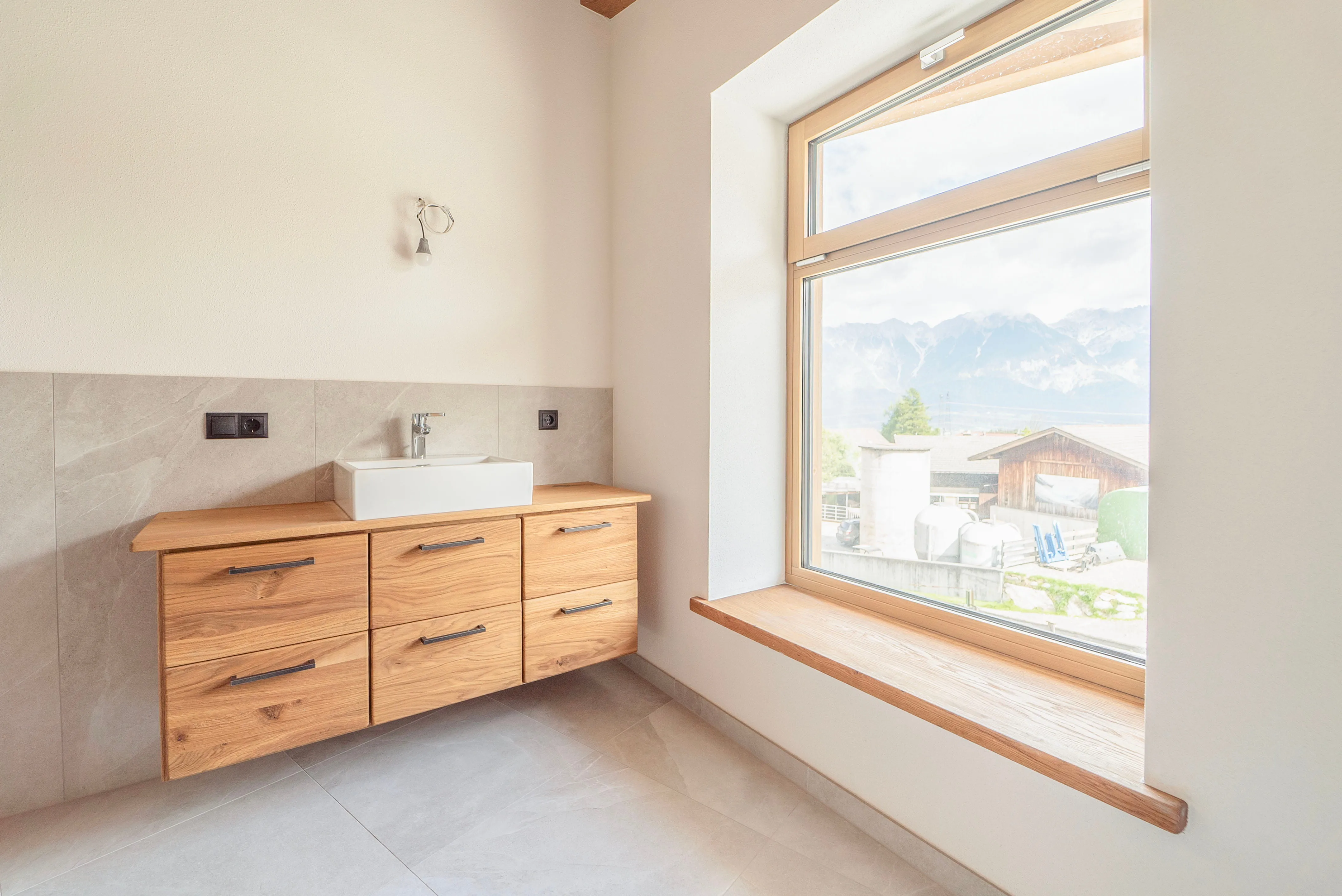 Helles Badezimmer mit hängendem Holzwaschbeckenunterschrank und großem Fenster mit Blick auf Berglandschaft.
