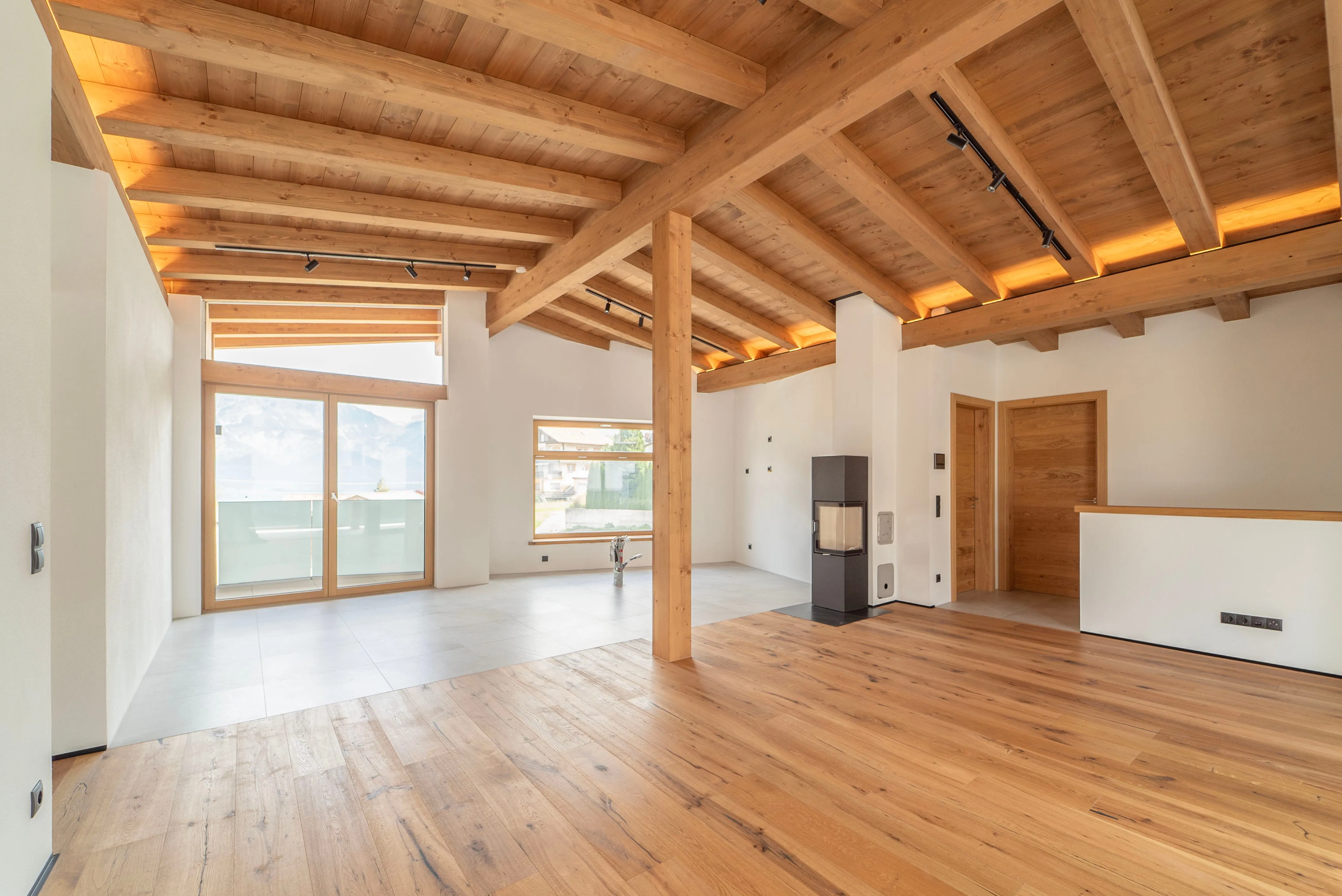 Helles, modernes Wohnzimmer mit sichtbaren Holzbalken an der Decke, großem Fenster mit Bergblick, Holzboden und Kamin.