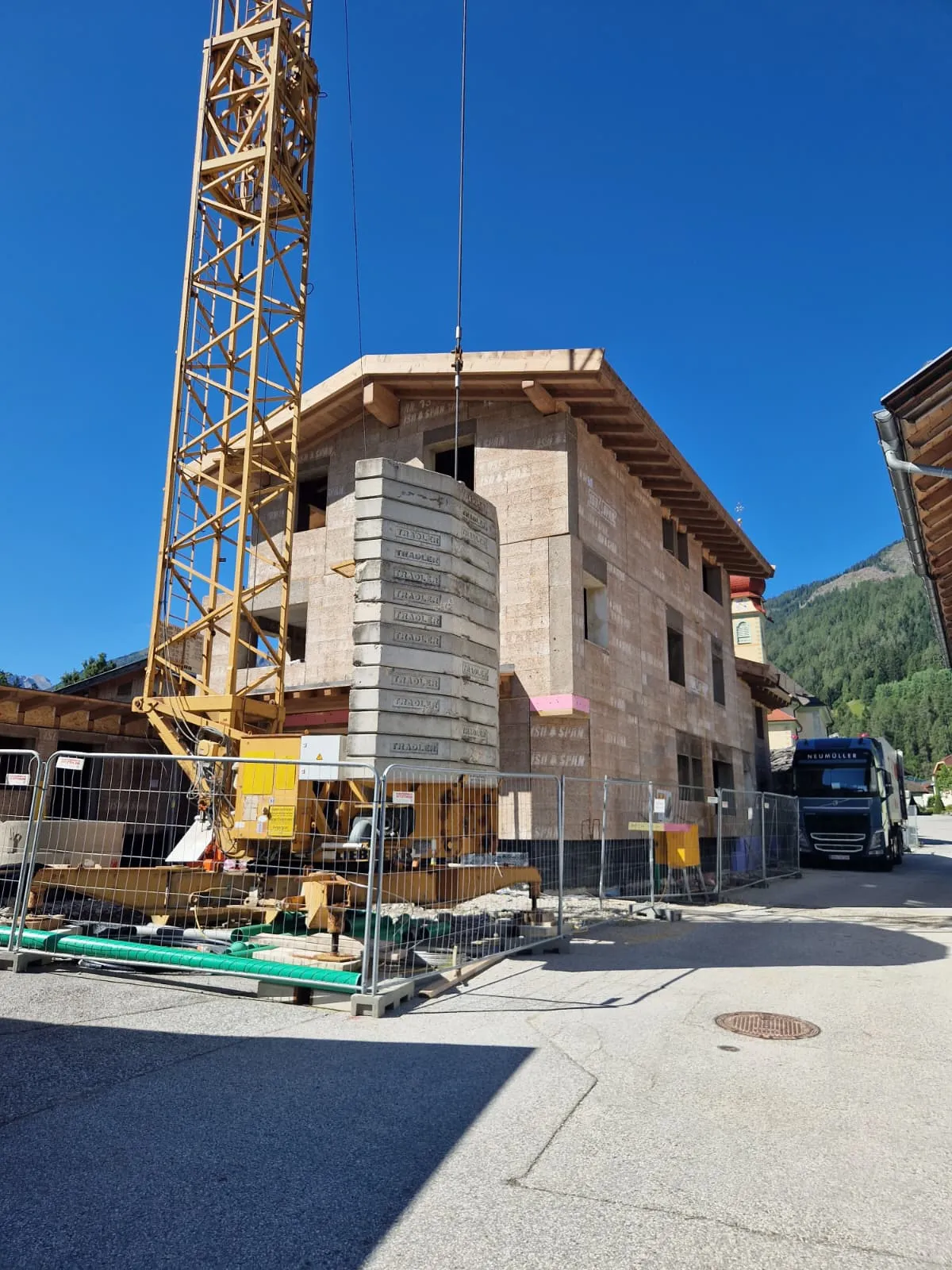 Baustelle eines mehrstöckigen Gebäudes mit Kran, Baugewichten und einem LKW unter blauem Himmel.