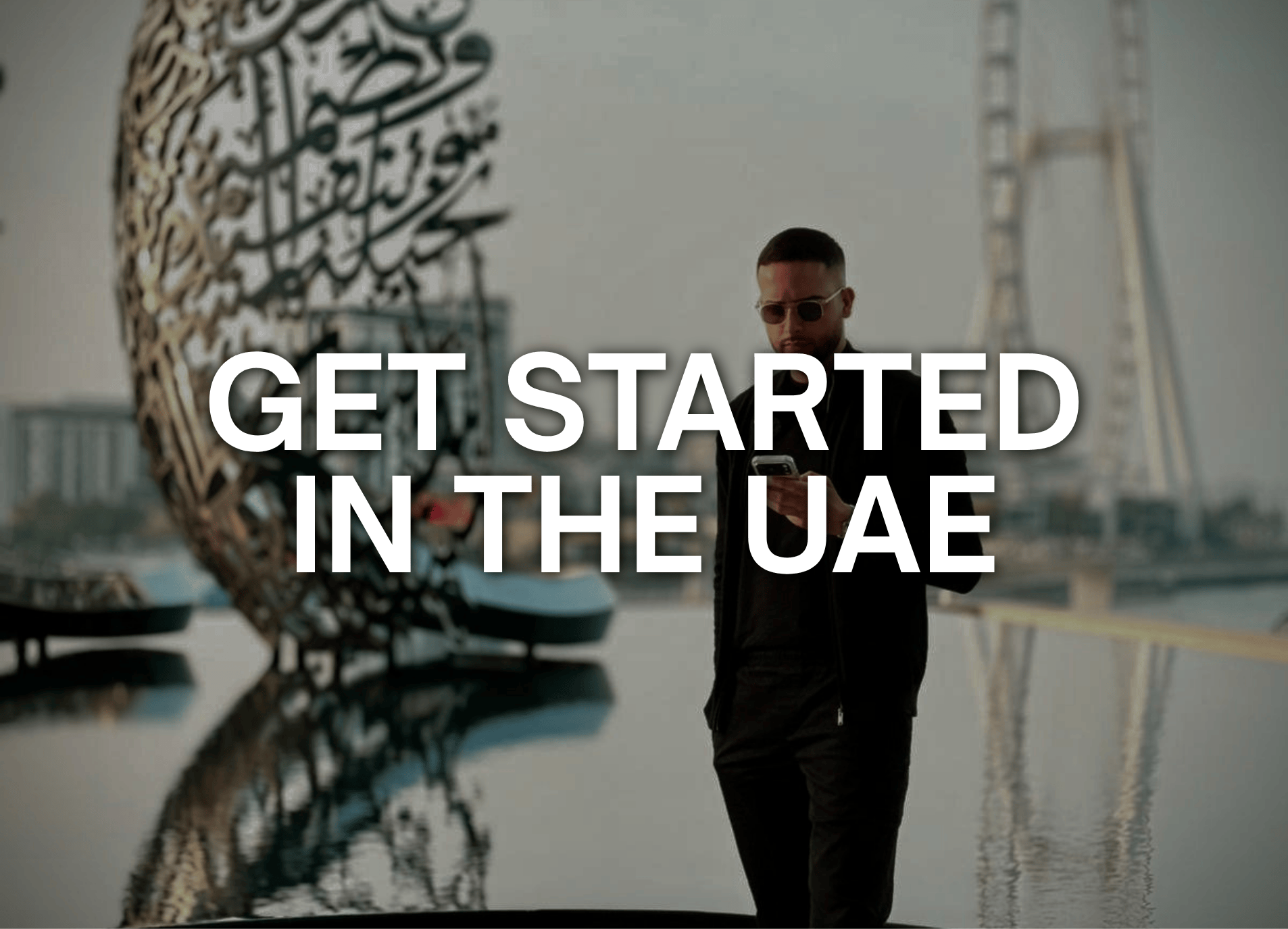 Man wearing sunglasses and dark clothing looking at his phone with a large sculpture and bridge in the background, overlaid with text 'Get Started in the UAE'.