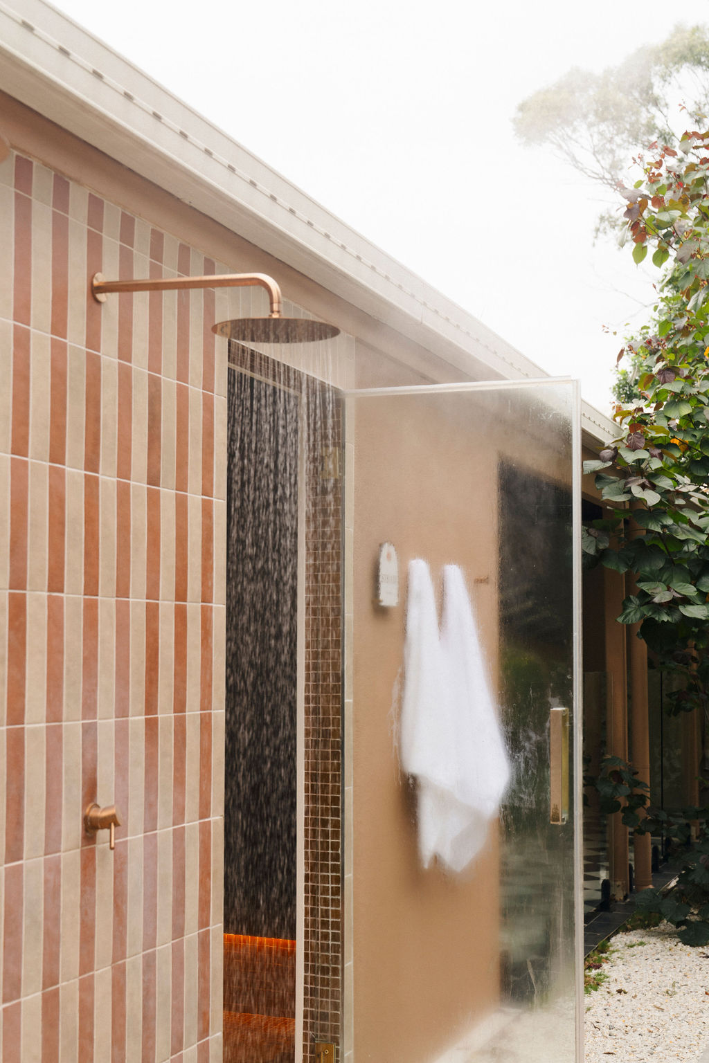 Outdoor shower with striped terracotta tiles and copper fixtures at Greenhouse Bathhouse