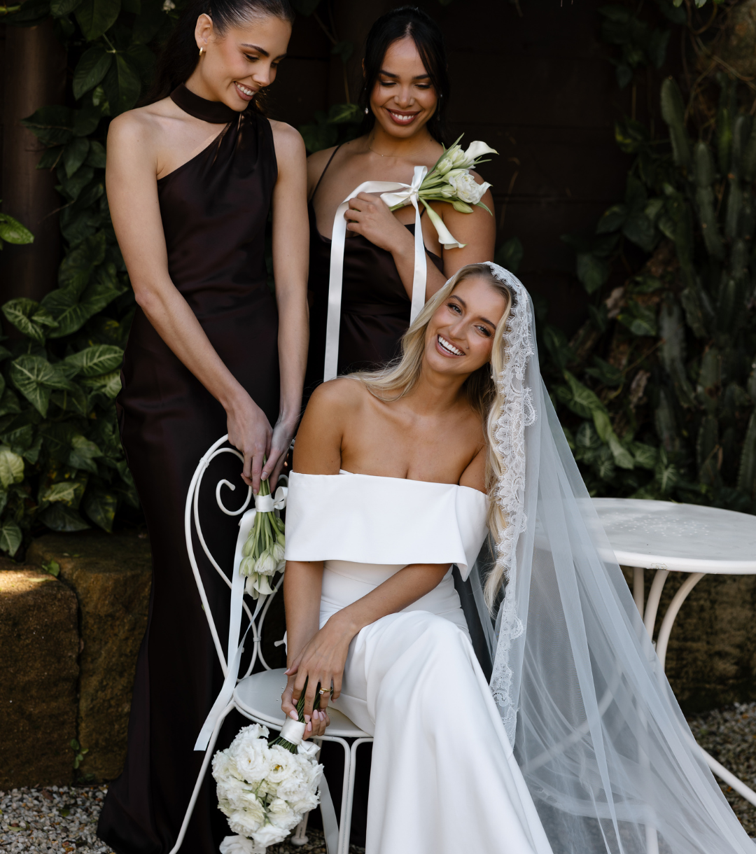 Bride in lace off-shoulder gown seated with bridesmaids in black gowns and white tulip bouquets at 268 Estate