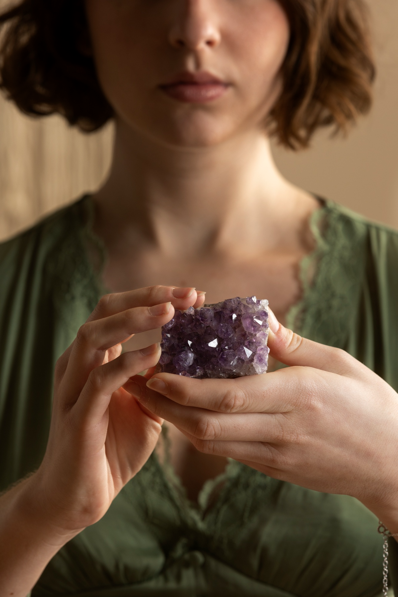 Close-up of a woman in a green dress holding a purple amethyst crystal cluster with both hands.