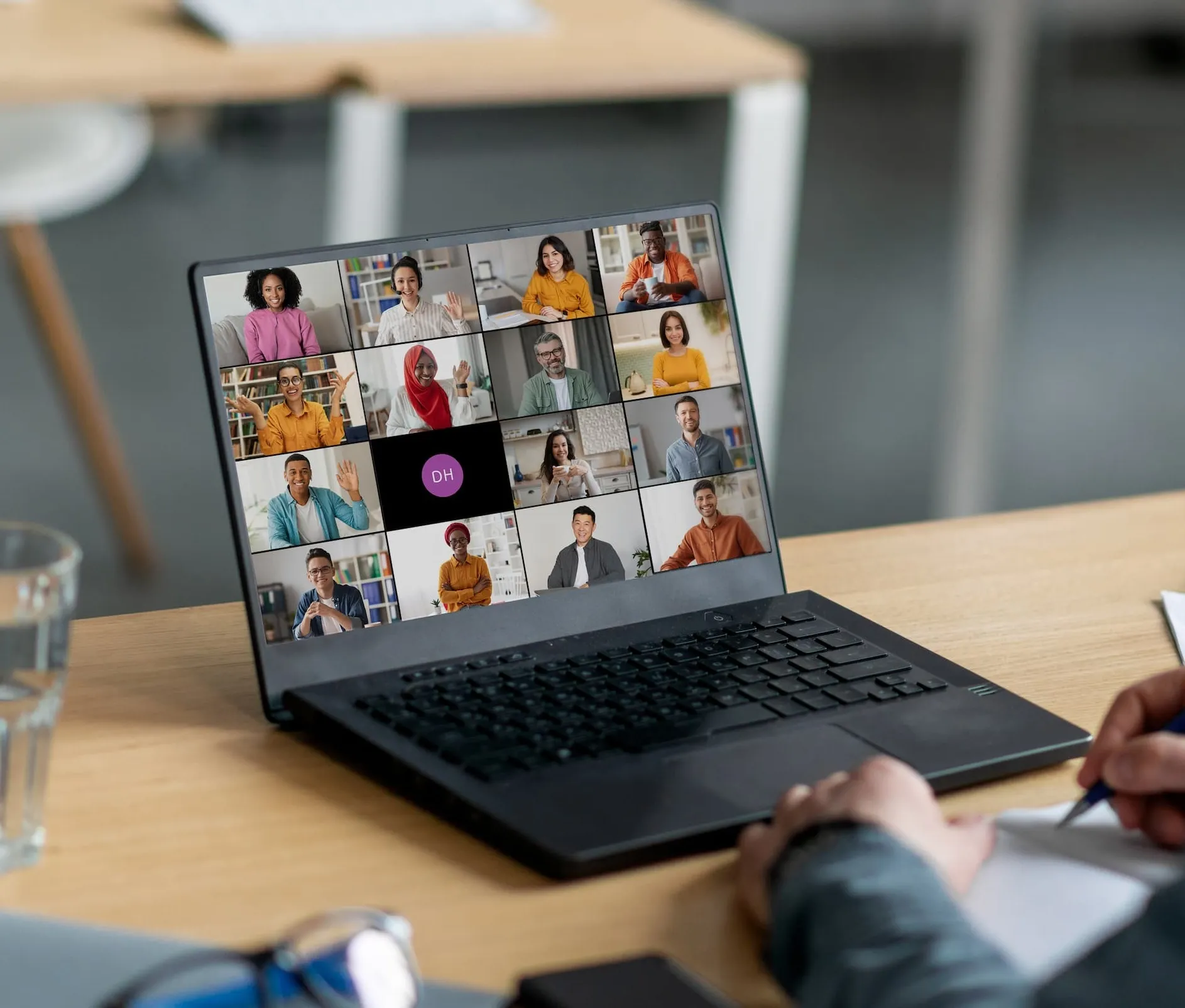 Ordinateur portable sur un bureau avec une visioconférence affichant quinze participants souriants et faisant signe de la main.