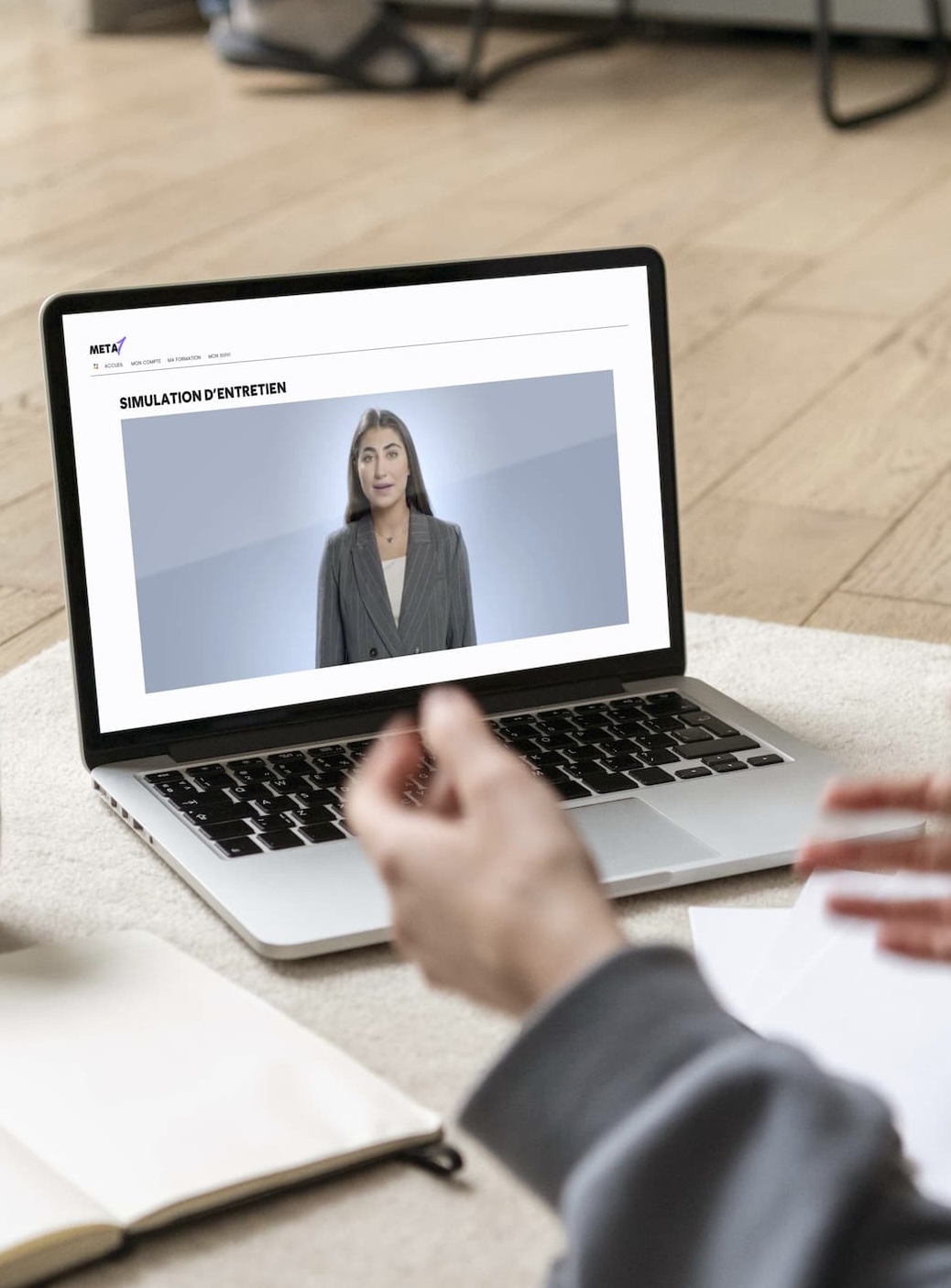 Personne suivant une simulation d'entretien d'embauche sur un ordinateur portable avec une femme en costume gris à l'écran.
