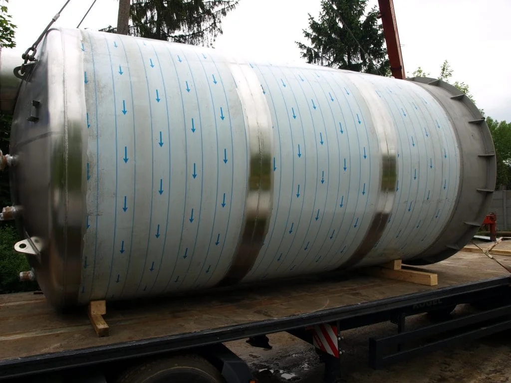 Duży stalowy zbiornik umieszczony poziomo na platformie ciężarówki na zewnątrz.