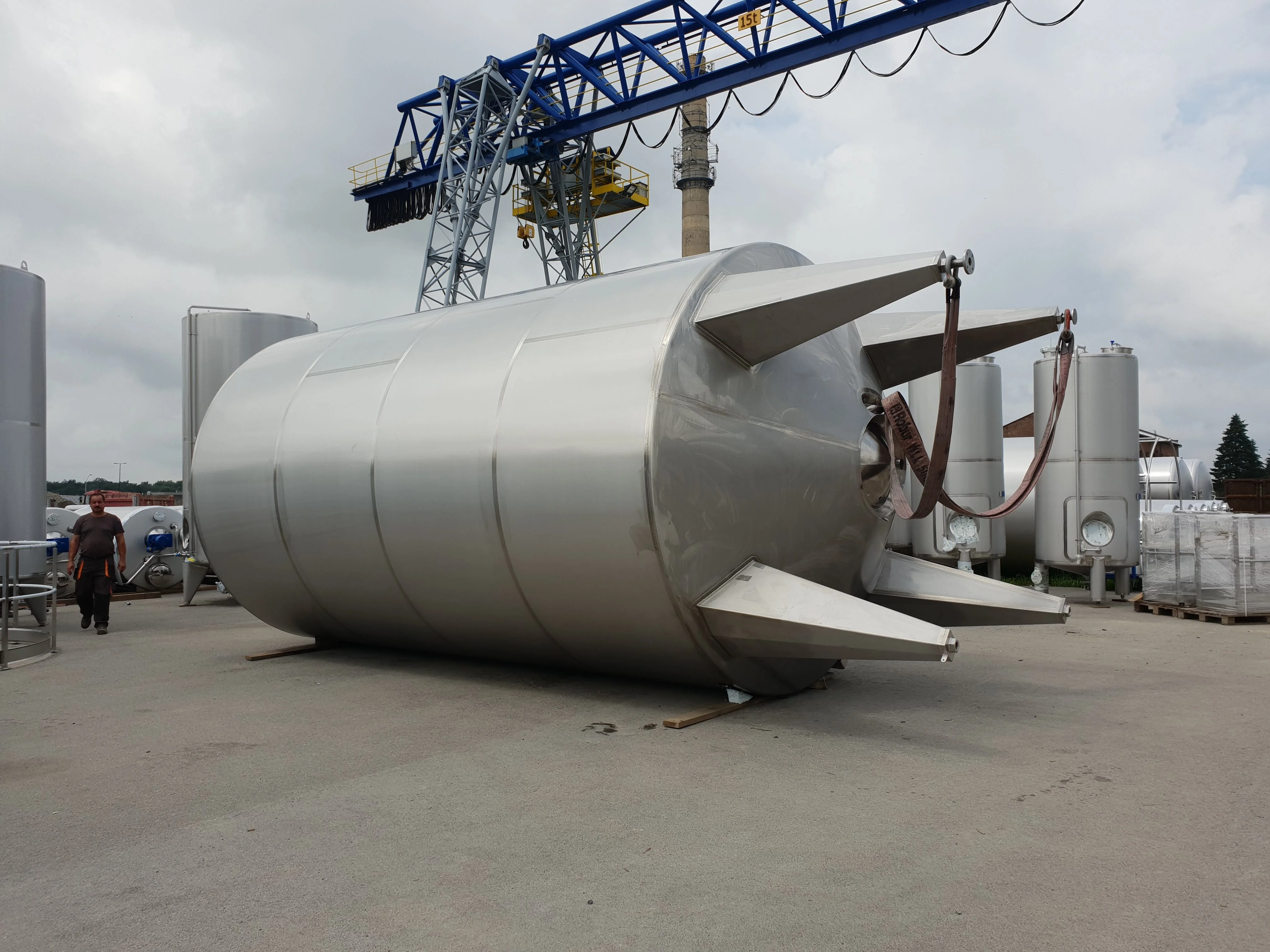 Wnętrze przemysłowego obiektu z dużym metalowym zbiornikiem i siecią rur ze stali nierdzewnej oraz metalową drabiną.