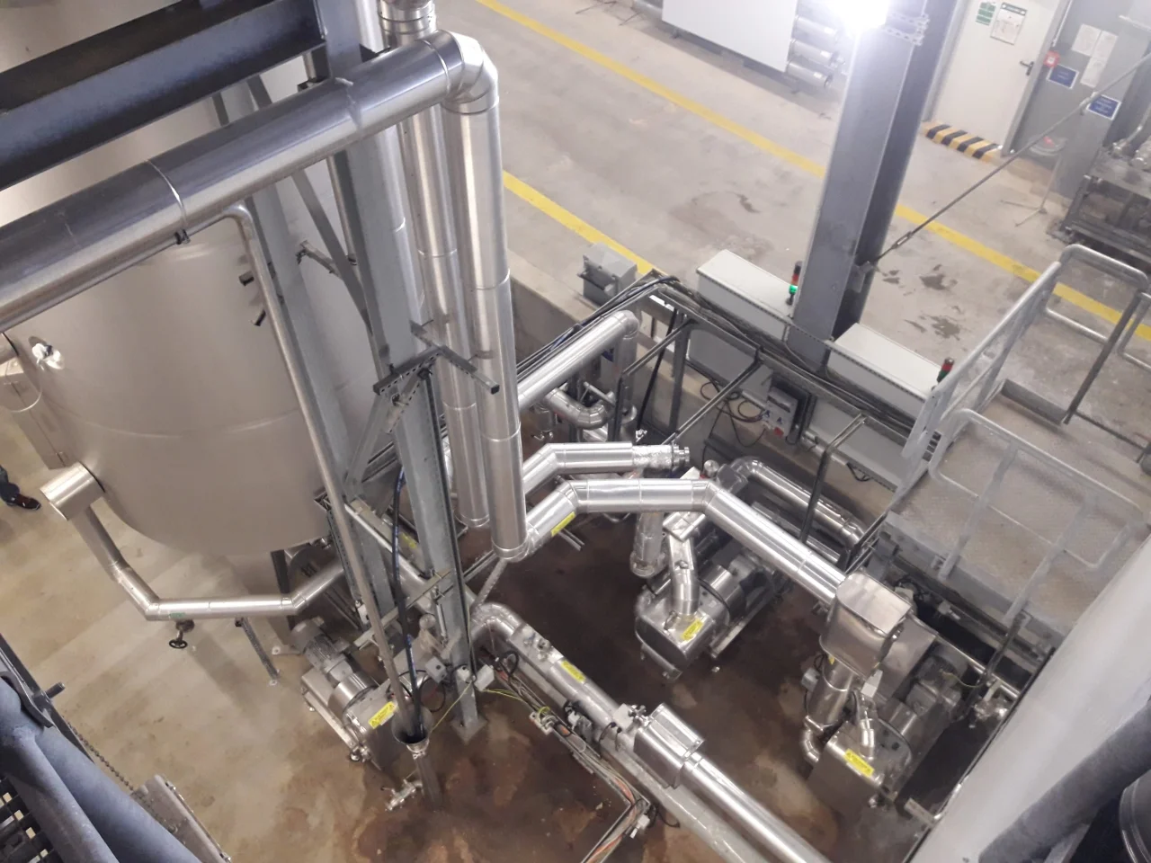 Widok z góry na przemysłową instalację z rurami i zbiornikami ze stali nierdzewnej w hali fabrycznej.