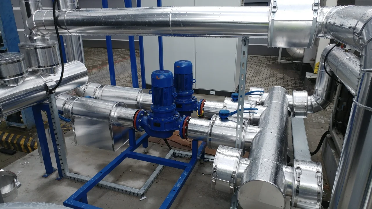 Zawory i rurociągi ze stali nierdzewnej oraz dwa niebieskie silniki elektryczne w instalacji przemysłowej.