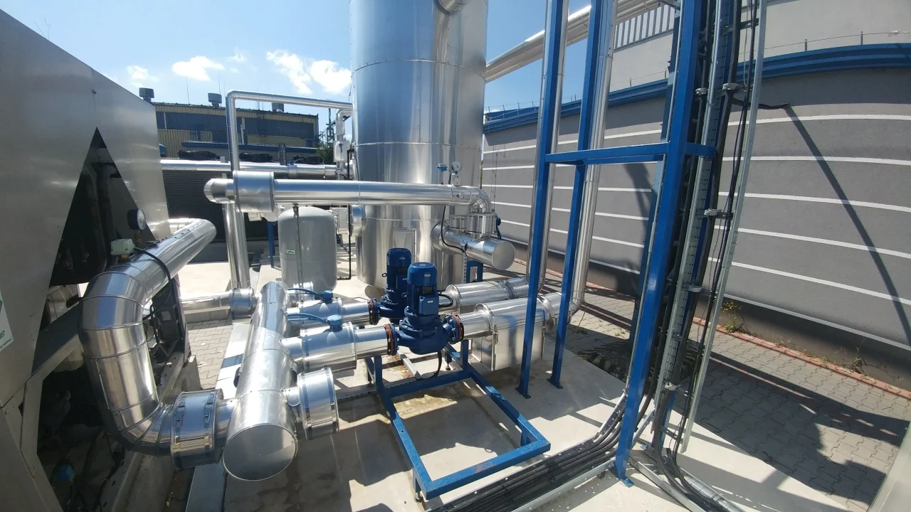 Instalacja przemysłowa z systemem rur ze stali nierdzewnej i niebieskimi pompami na betonowej podstawie na zewnątrz.