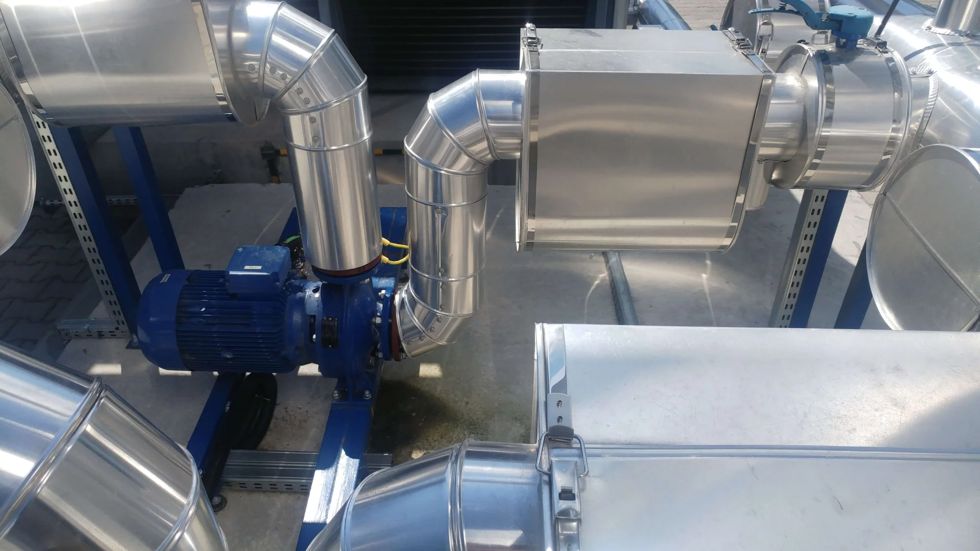 Przemysłowy system wentylacyjny z metalowymi kanałami i niebieskim silnikiem elektrycznym.