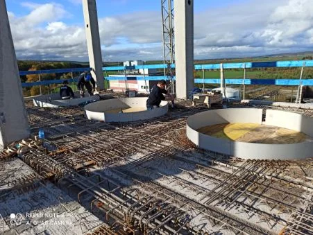 Na placu budowy dwie osoby pracujące przy zbrojeniu na stropie z widokiem na ogrodzenie i krajobraz pod niebieskim niebem.