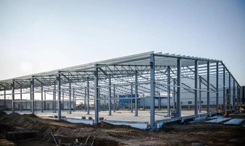 Konstrukcja stalowa hali magazynowej w trakcie budowy na placu budowy oświetlonym przez światło dzienne.