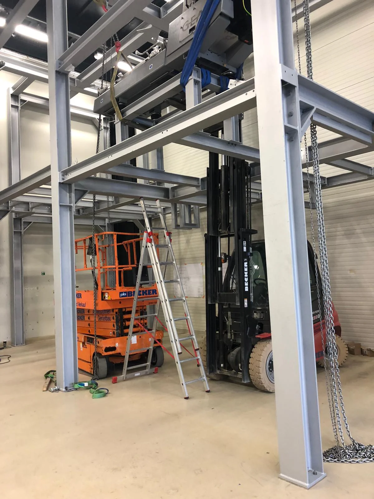 Hala przemysłowa z rusztowaniem stalowym, drabiną oraz wózkiem widłowym i podnośnikiem nożycowym.