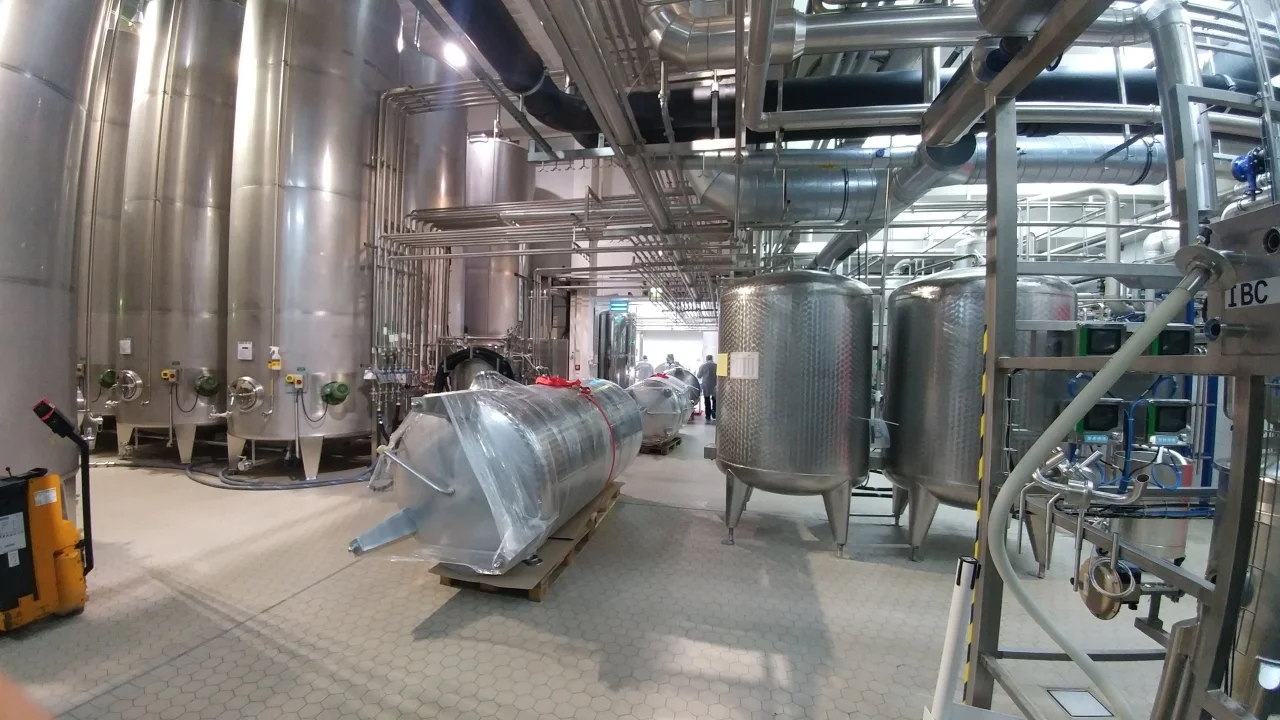 Wnętrze nowoczesnej hali produkcyjnej z dużymi, stalowymi zbiornikami i instalacjami rurowymi.