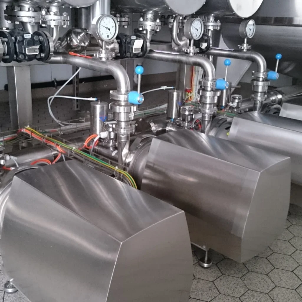 Bloki ze stali nierdzewnej i rurki z manometrami oraz niebieskimi pokrętłami w przemysłowej instalacji rurowej.