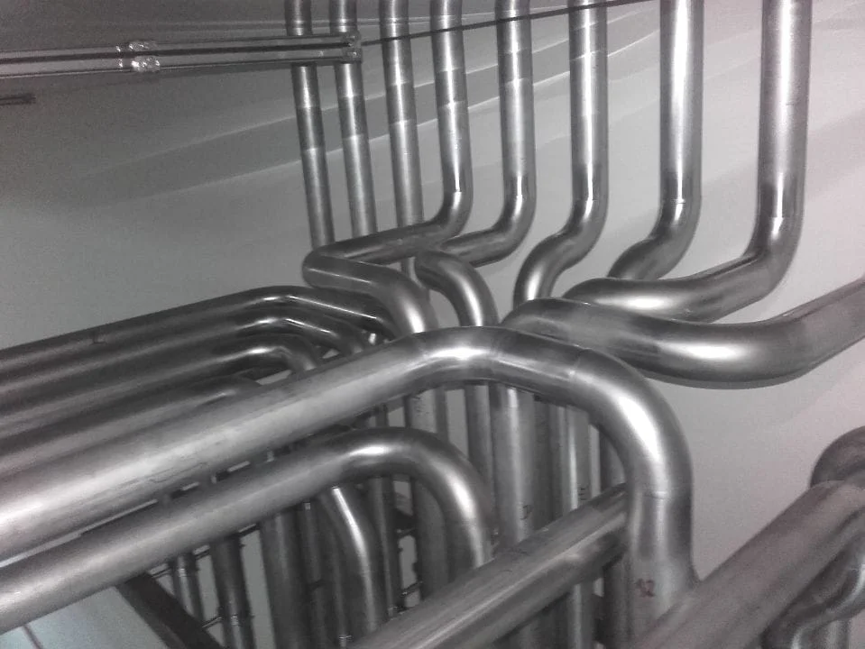 System metalowych rur zgiętych pod kątem w pionowej instalacji przemysłowej.