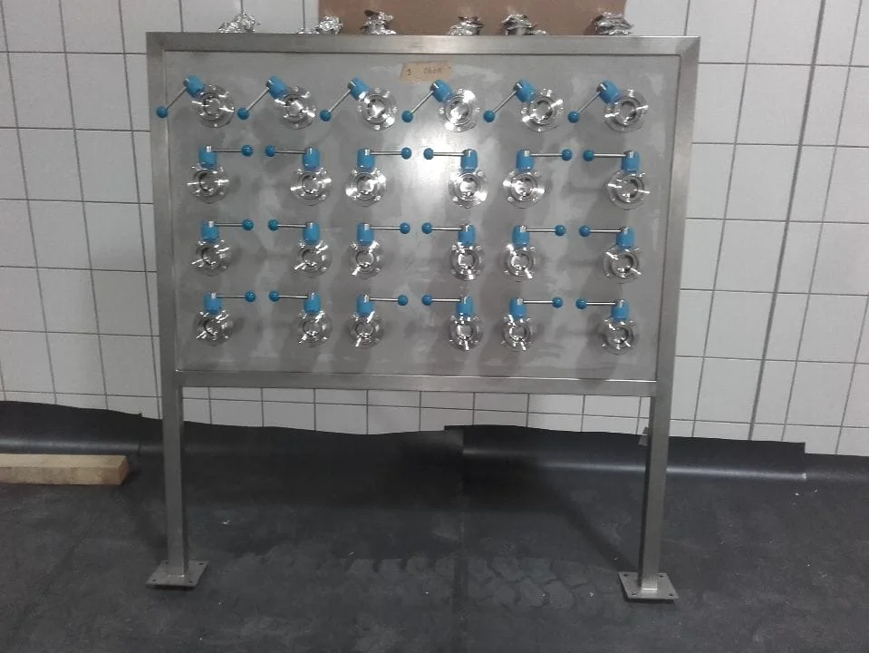 Duży przemysłowy zbiornik ze stali nierdzewnej z rurami i zaworami w białym, kafelkowym pomieszczeniu.