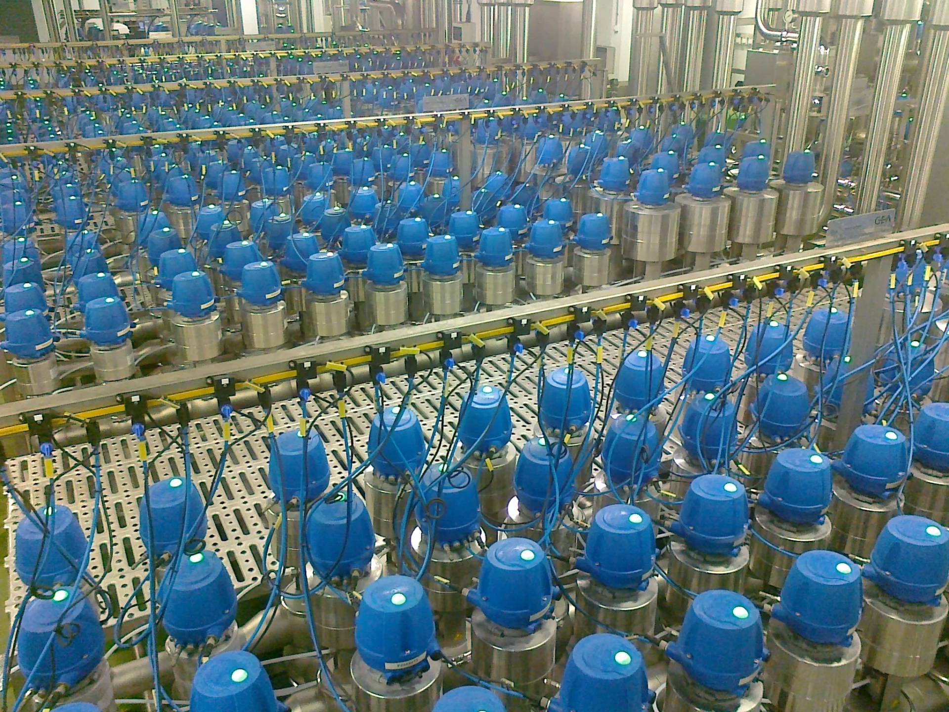 Wielorzędowy układ przemysłowych zaworów z niebieskimi głowicami i kablami w zakładzie produkcyjnym.