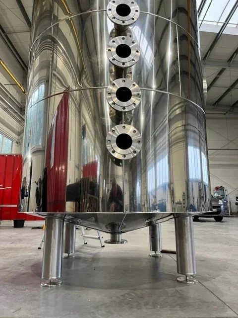 Metalowe części rurociągowe i złączki spoczywające na drewnianej palecie w warsztacie.