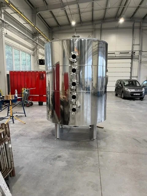 Duży srebrny cylinder ze stali nierdzewnej stojący na nogach w hali warsztatowej.