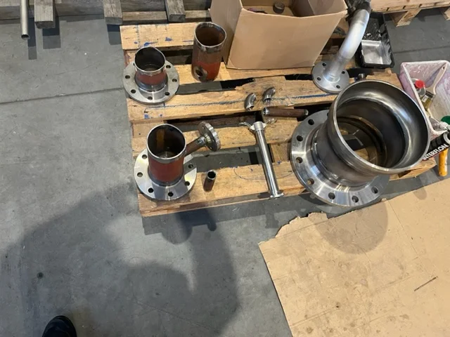 Metalowe części rurociągów i złącza na drewnianej palecie w warsztacie.