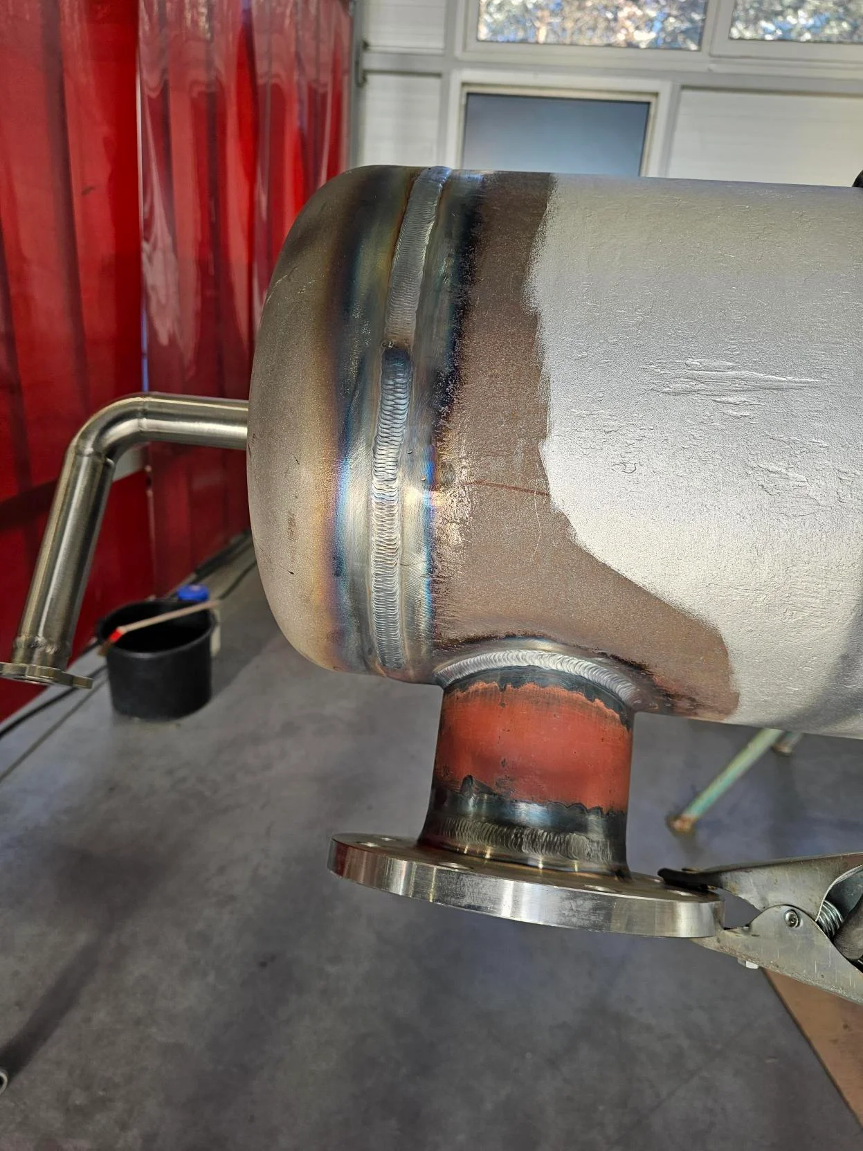 Metalowy zbiornik z widocznym spawem i przyspawanym króćcem z kołnierzem w warsztacie.