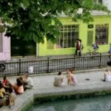 Des personnes assises au bord de l'eau le long d'un canal à Paris, face à une devanture de boutique vert pomme, dans l'esprit des quartiers vivants d'Anchor.