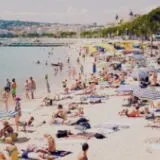Plage de sable ensoleillée et animée à Cannes, bordée par la mer et des parasols, illustrant le cadre des destinations estivales Anchor.