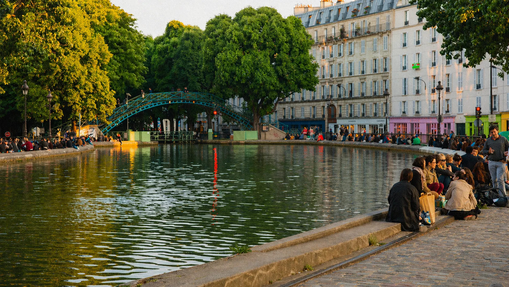 Scène de fin de journée ensoleillée au bord du canal Saint-Martin à Paris, où habitants et voyageurs partagent un moment de détente au fil de l'eau, illustrant l'art de vivre parisien proposé par Anchor Living Apartments.