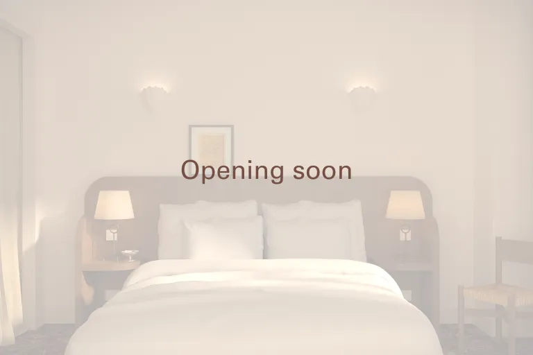 A high-end double room from Anchor, bathed in soft light. A large bed with crisp white linens faces a dark upholstered headboard, flanked by two bedside tables with lit lamps. The text "Openi" is displayed in translucent panels.