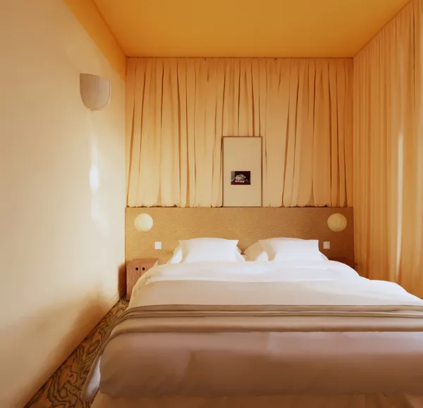 Una camera da letto contemporanea monocromatica nei toni del giallo e del beige in un prestigioso indirizzo di Anchor a Parigi, caratterizzata da tende con texture particolari e un letto minimalista.