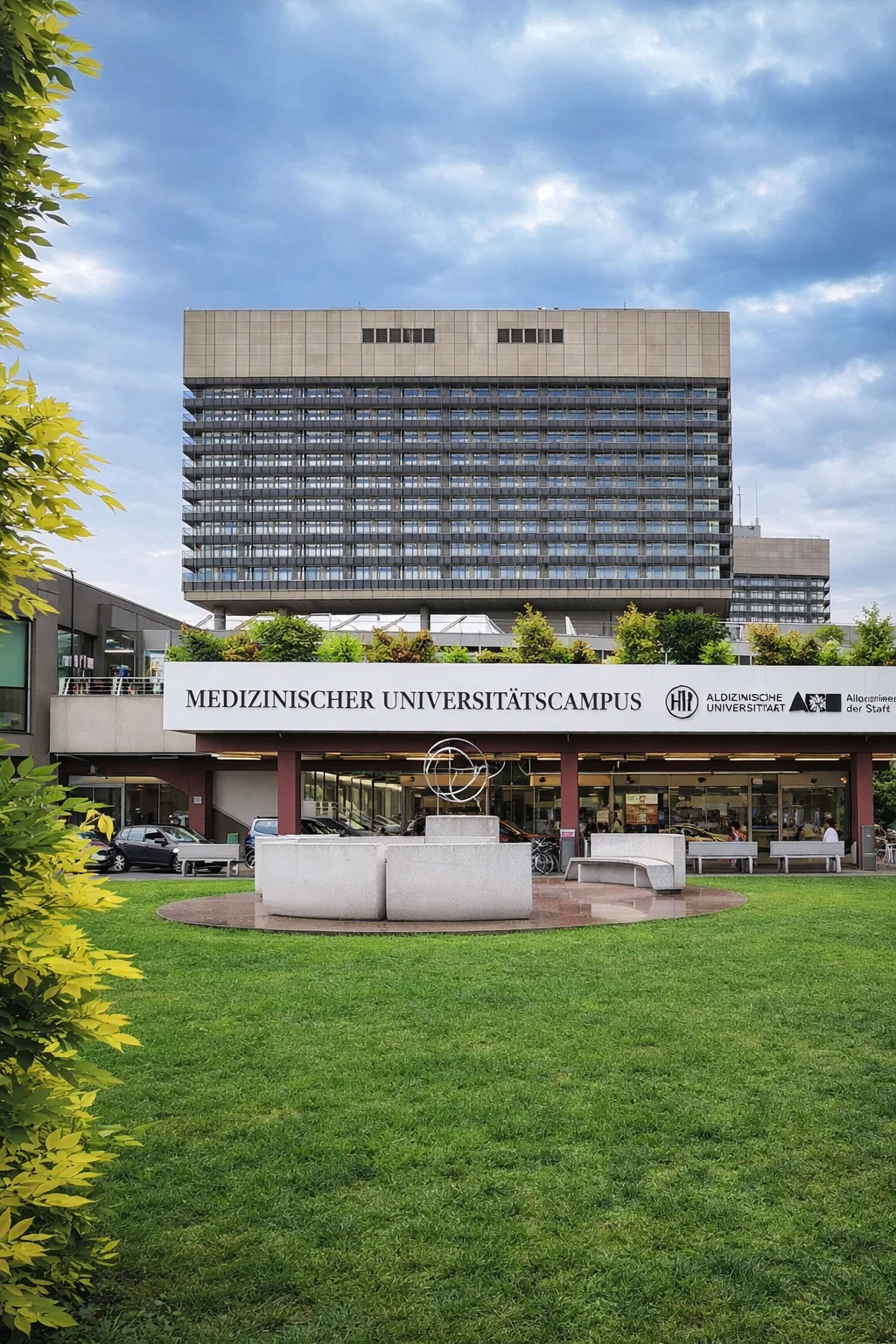 Medizinischer Universitätscampus building with a modern tower and green lawn in front under a cloudy sky.