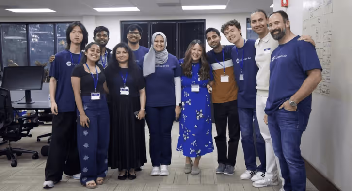 A diverse group of ten people standing closely together in an office, smiling towards the camera.
