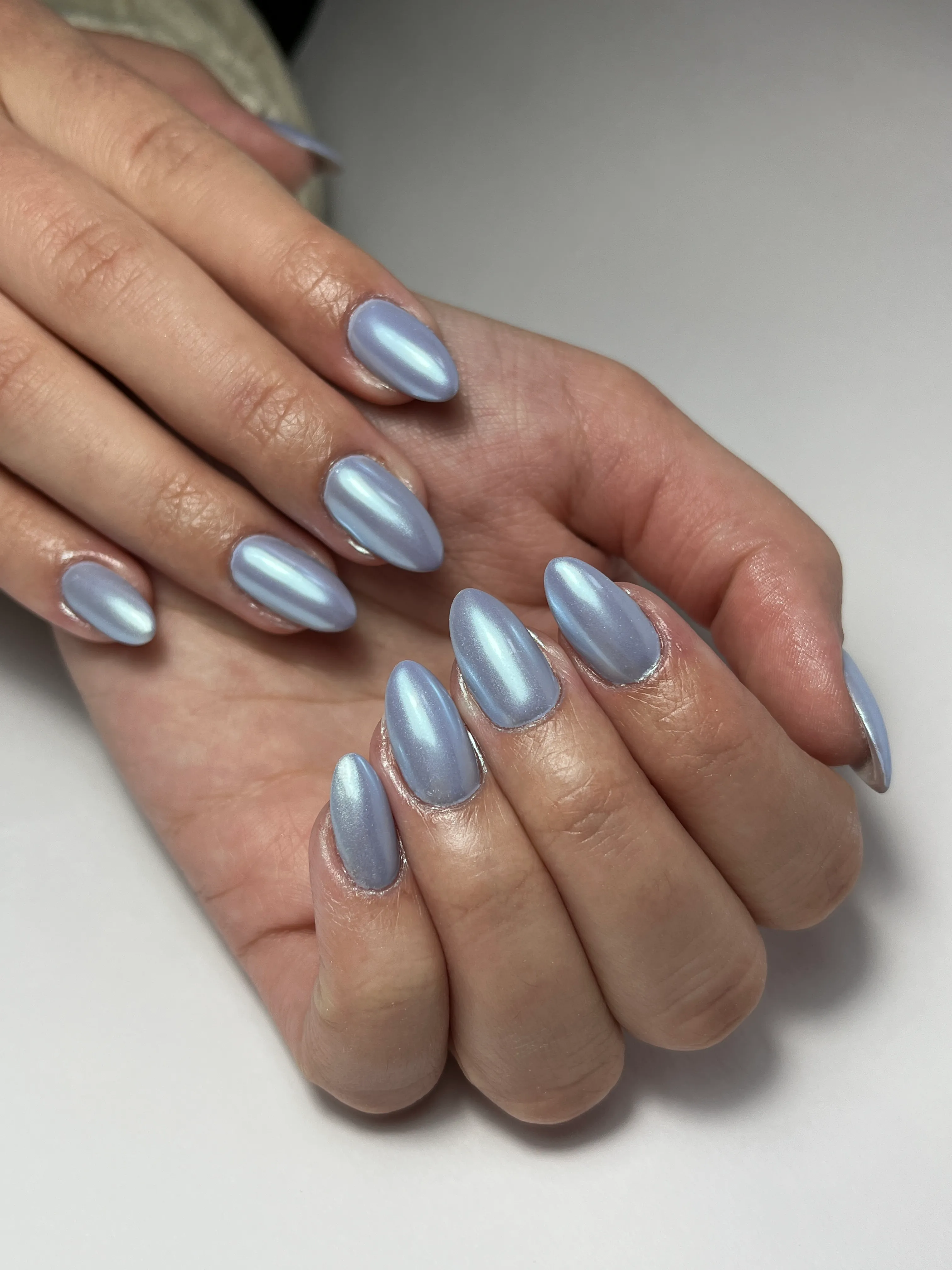 Hands with almond-shaped nails painted in shiny light blue metallic polish.