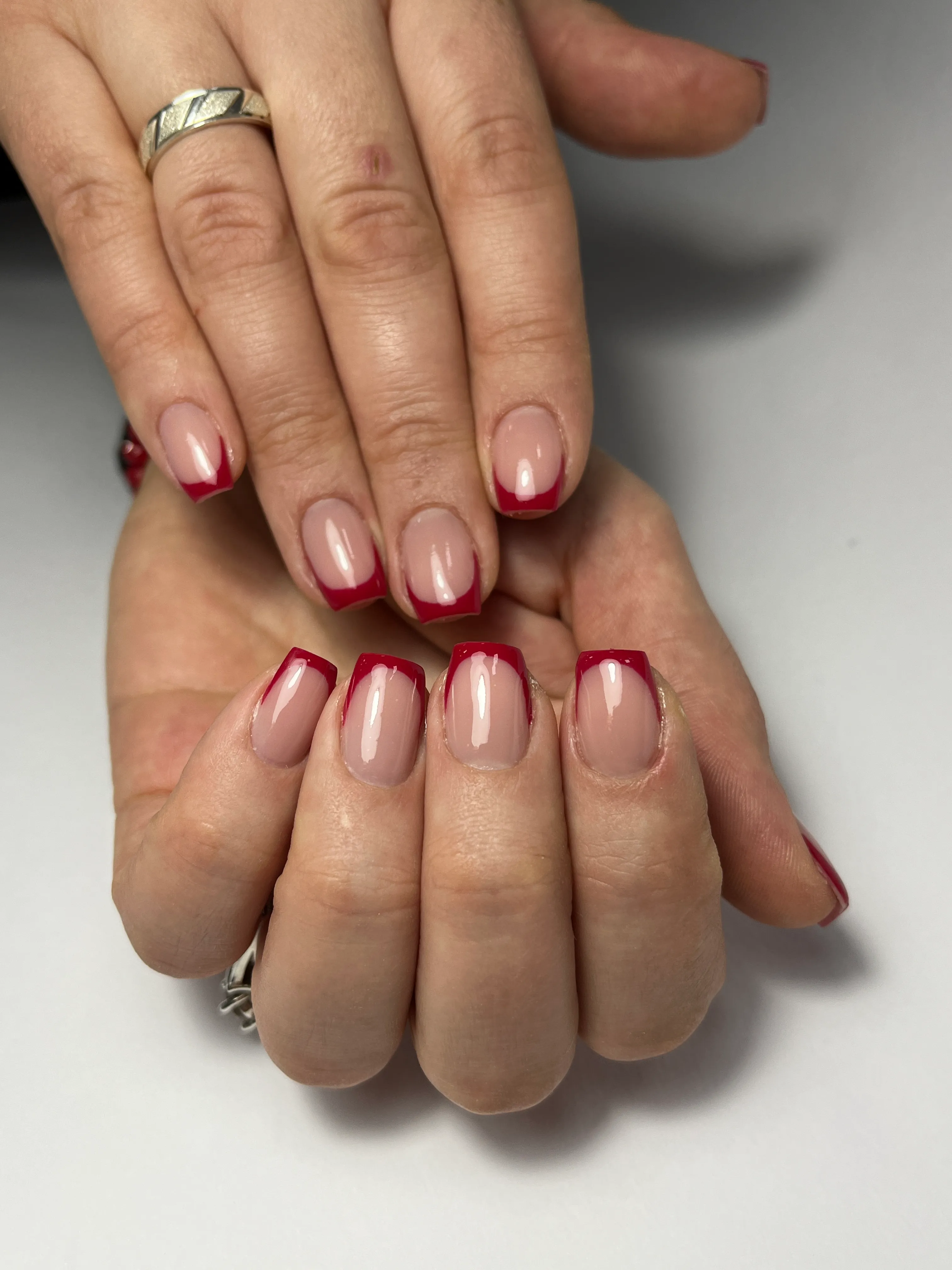 Hands with neatly manicured nails featuring nude polish and red French tips.