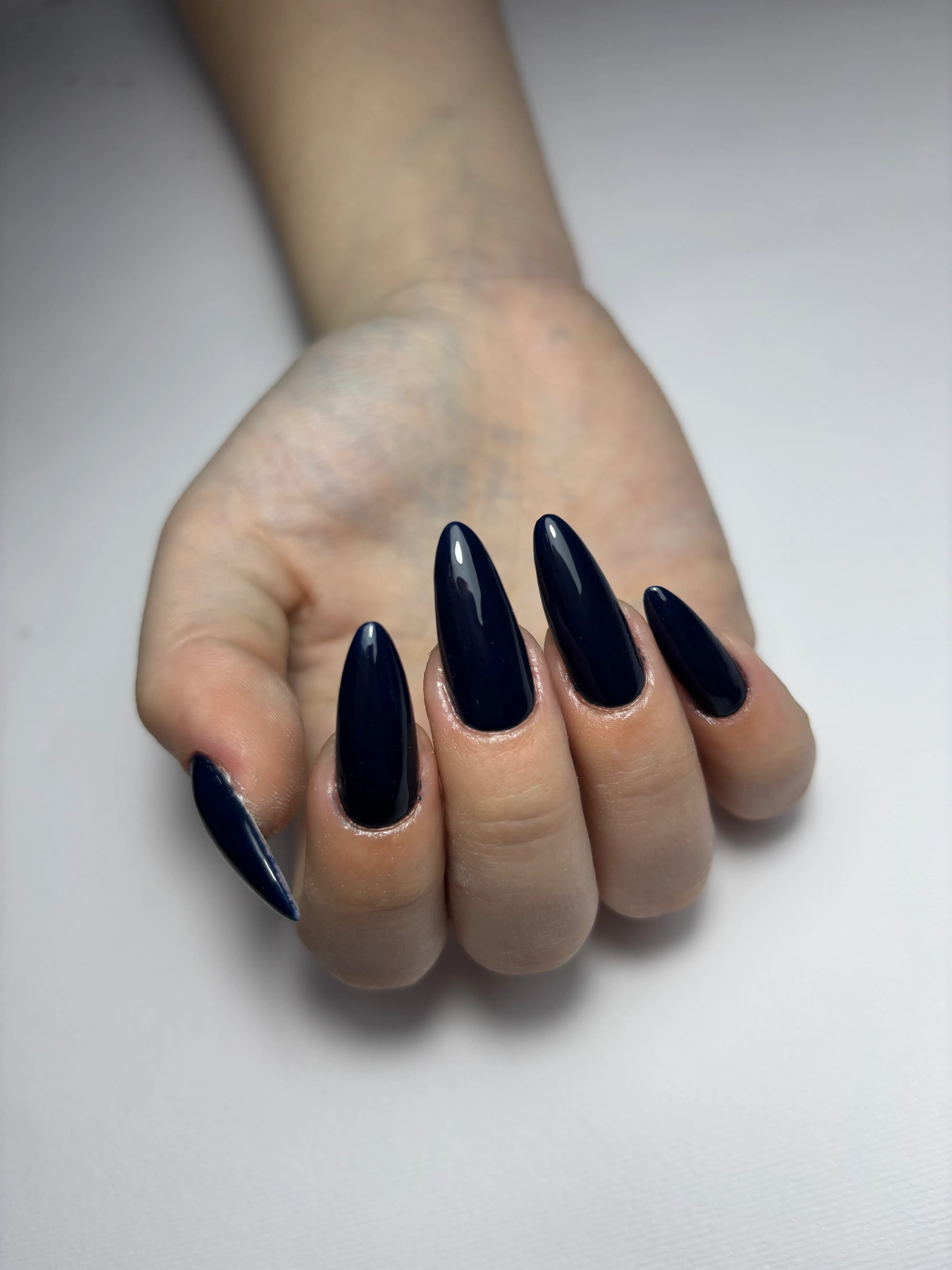 Hand with long, glossy black almond-shaped acrylic nails against a white background.