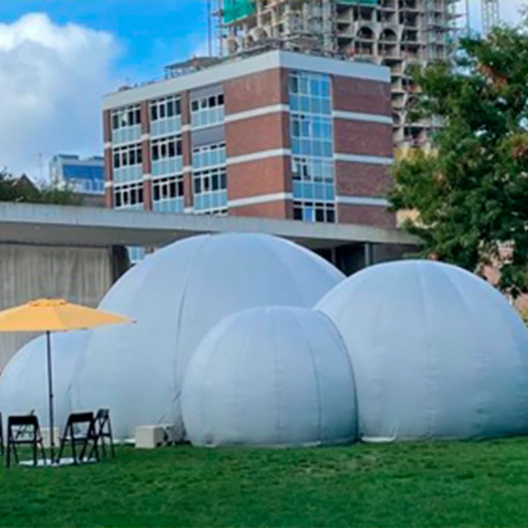 A cluster of white inflatable dome tents set on grass near urban buildings on a clear day.