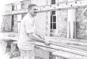 Man smiling and working with wooden planks at a construction site with a stone wall in the background.